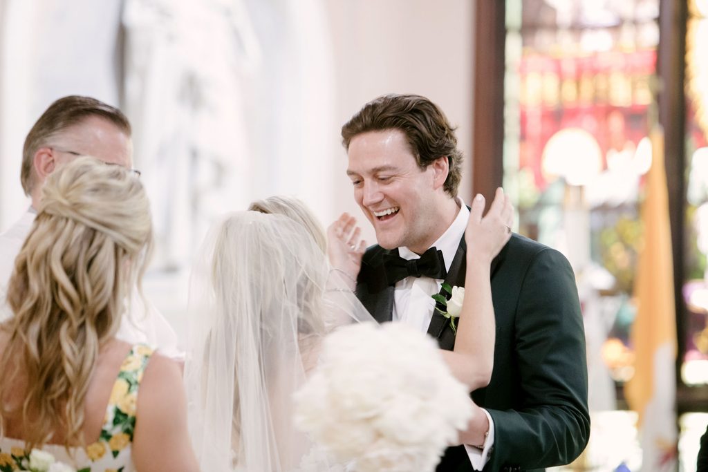 Groom laughing joyfully as his bride in a veil stands close to him during their wedding ceremony