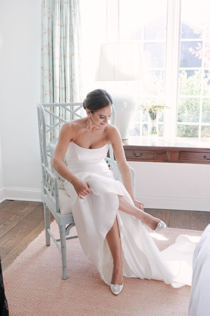 Bride sitting in a chair putting on her wedding shoes during unhurried getting-ready portraits