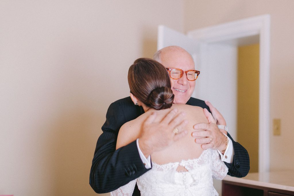 Bride in lace wedding gown embracing her father, who is smiling with his eyes closed, before the ceremony