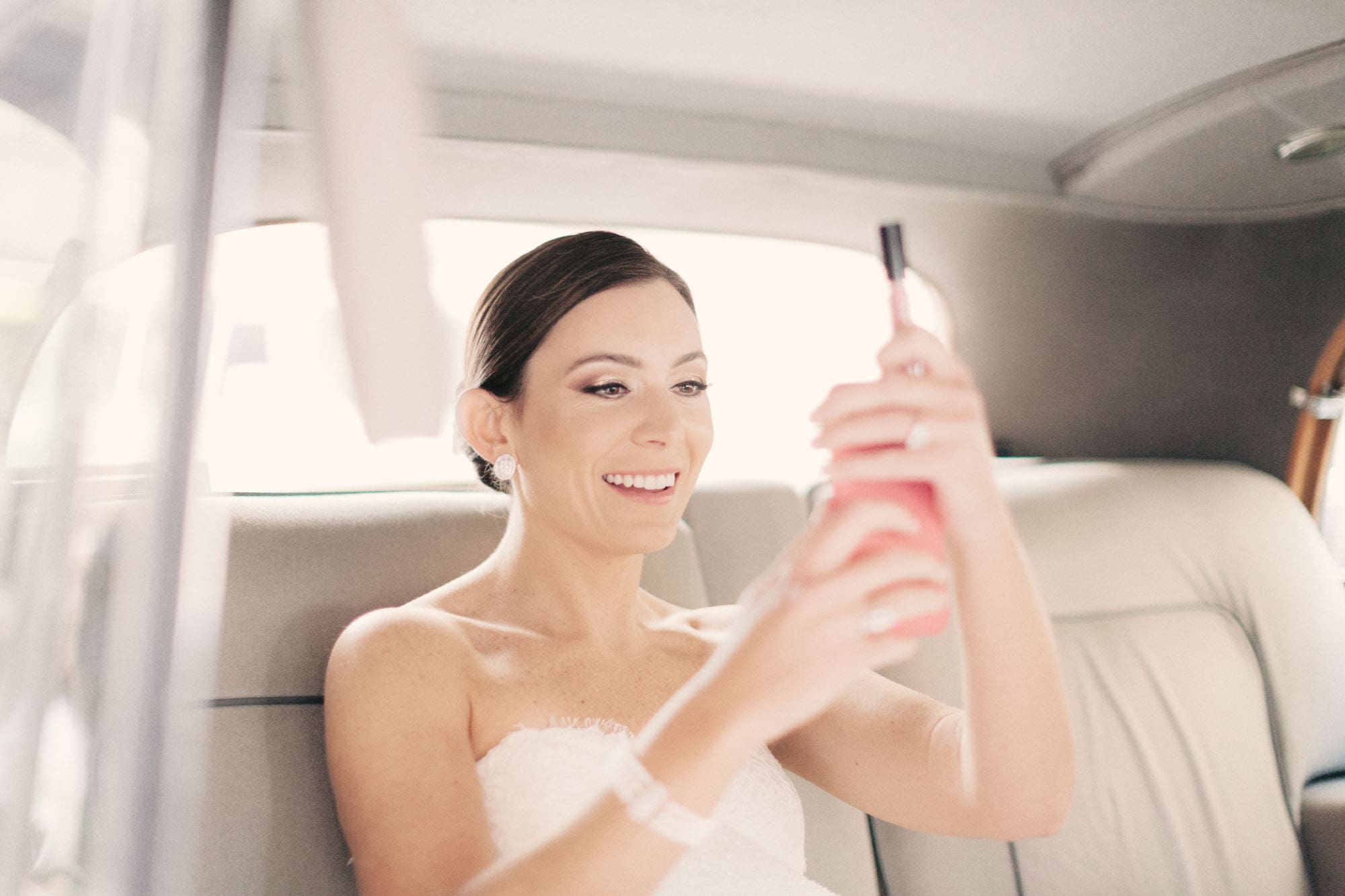 Bride smiling candidly at her phone in the car on her wedding day, photographed by a Wayne, PA wedding photographer, Sarah DiCicco