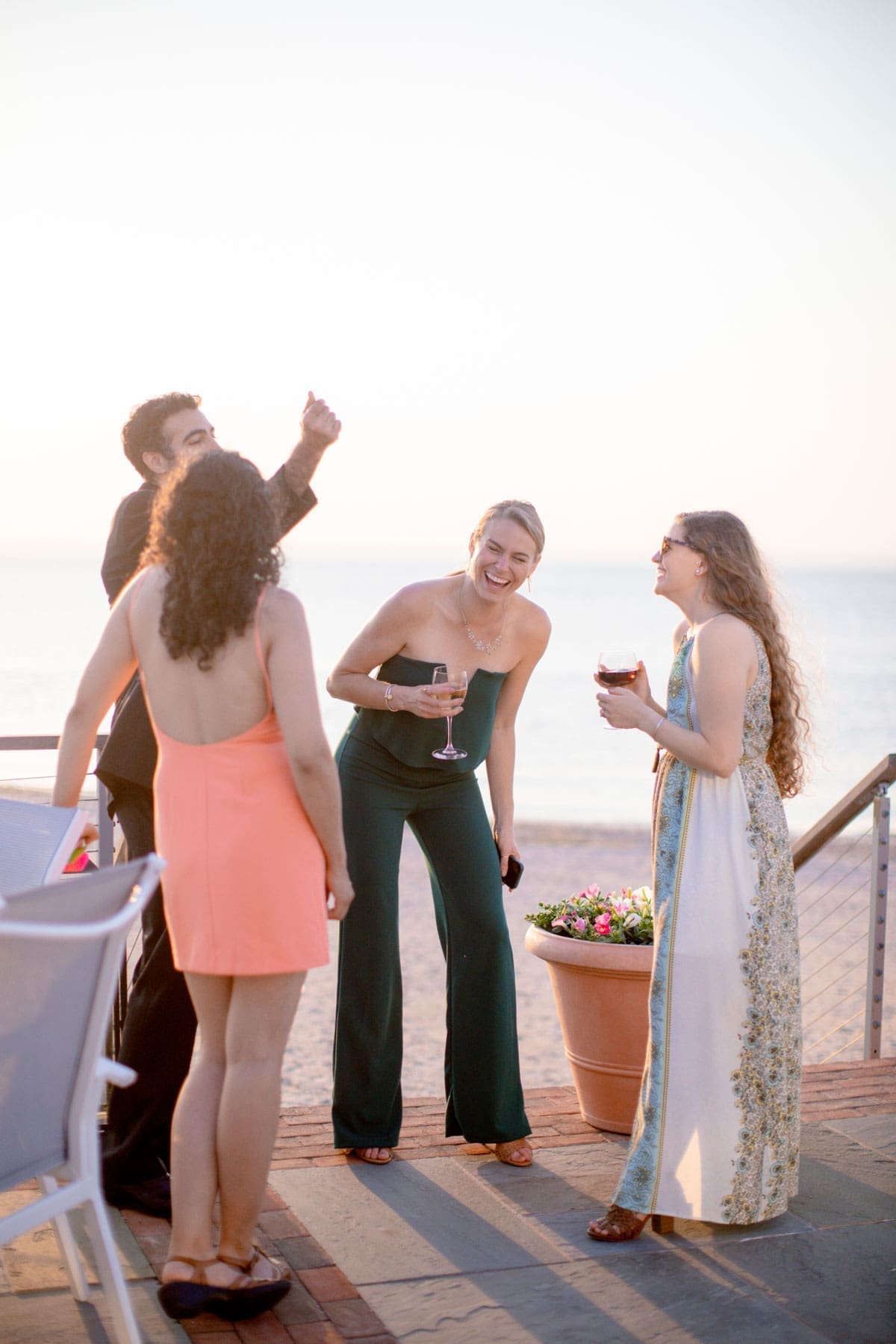 Wedding guests laughing together during cocktail hour at sunset by the beach